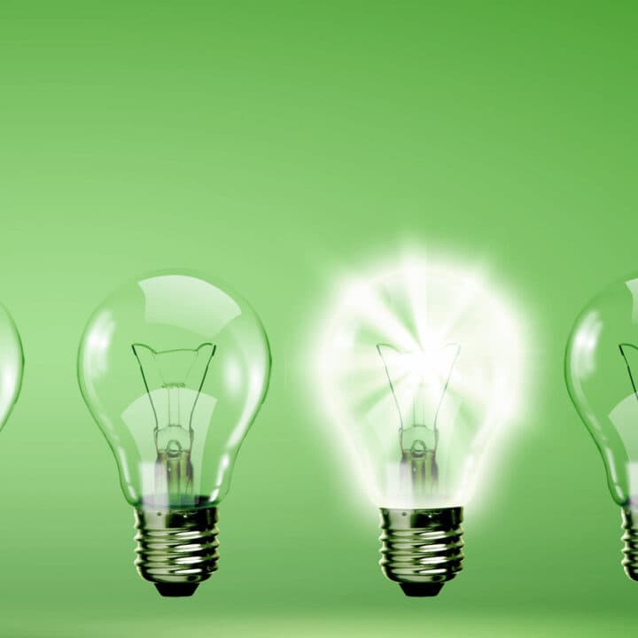 En glödlampa som lyser mot grön bakgrund, bredvid är lamporna släckta