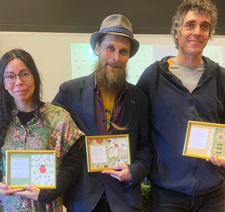 Tre personer står på rad och har precis tagit emot ett diplom i guldram