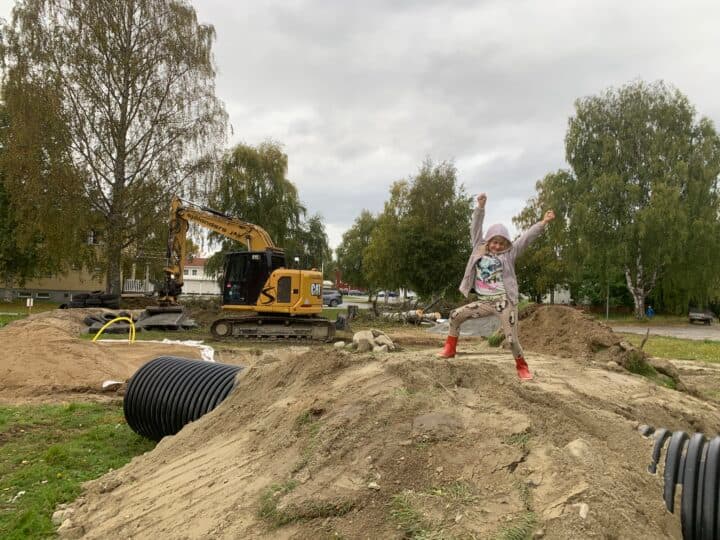 Stora jordhögar, en grävmaskin i fjärran, ett barn stoltserar på en kulle i förgrunden